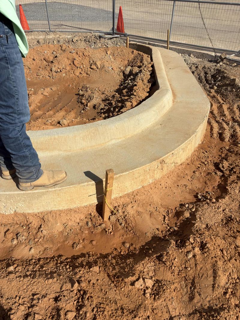 Freshly poured curved concrete curb wrapping around a dirt island