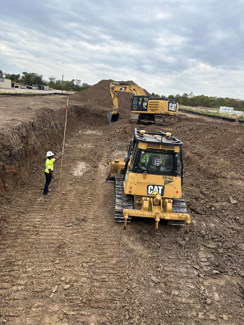 Dozer and a crew member in hi-vis inside a deep excavation, with an excavator on the stockpile behind